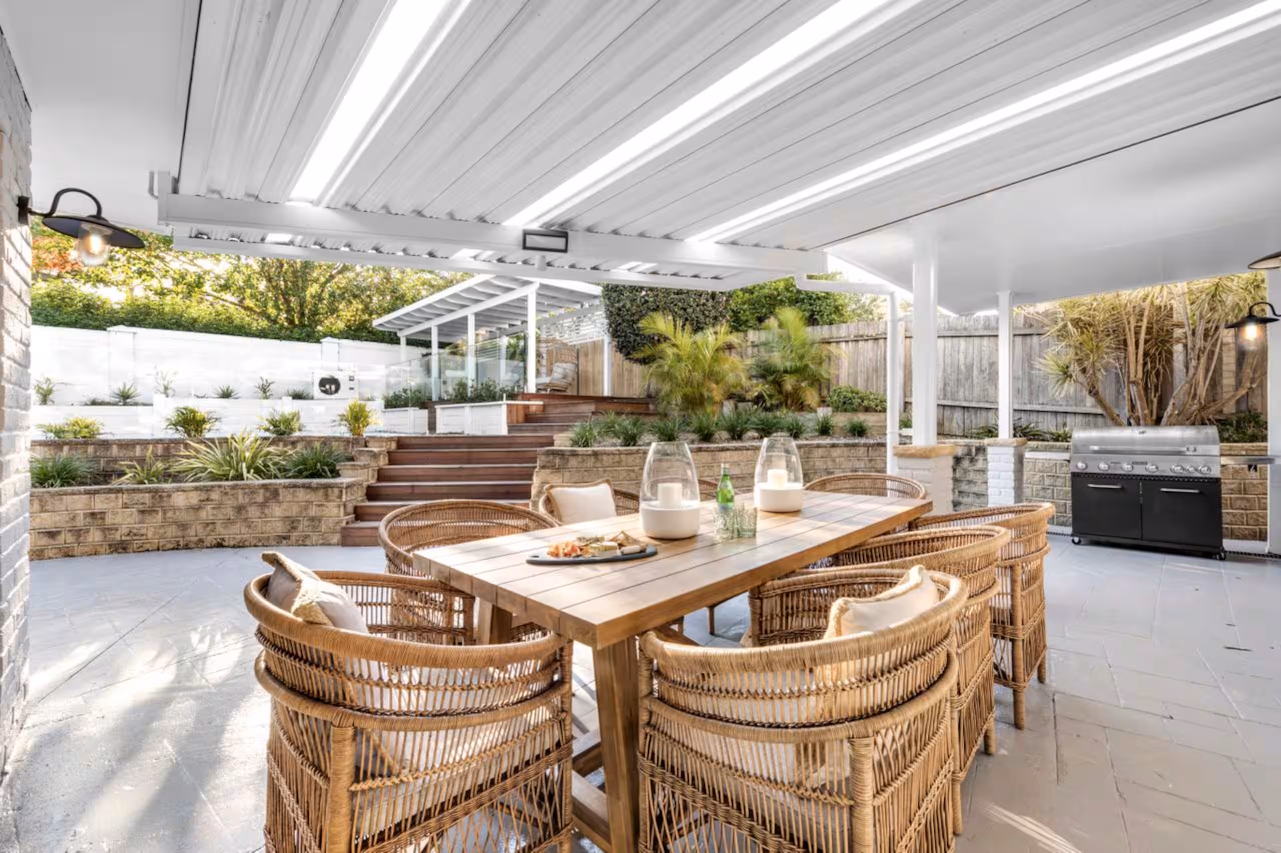 Covered alfresco dining with a long timber table, rattan chairs and a built-in BBQ.
