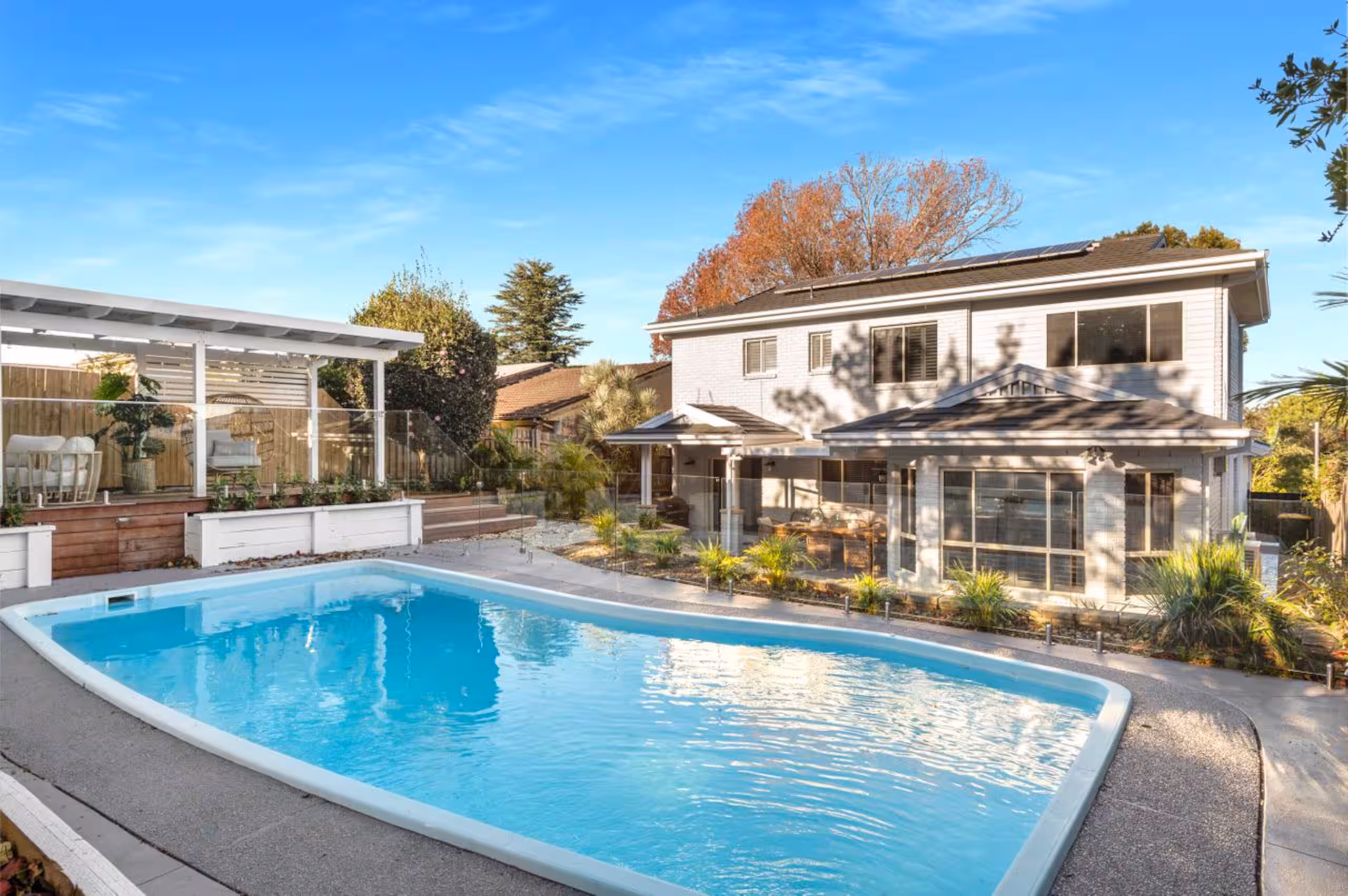 The backyard heated swimming pool with the home and pergola beyond, under a clear sky.
